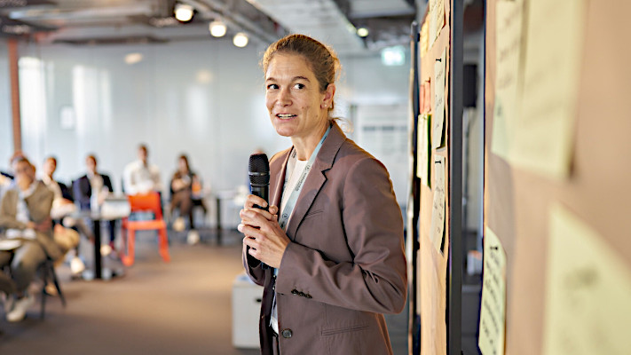 Moderatorin mit Mikrofon und Pinnwand bei einer Sustainable-Arbeitsrunde